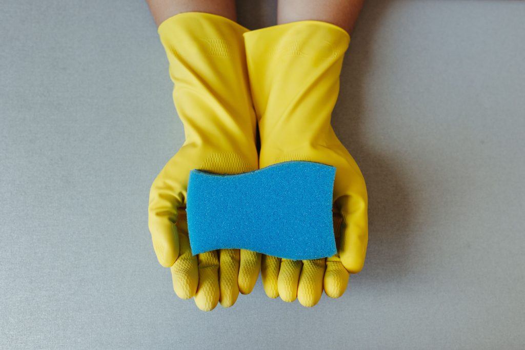 Vue de dessus moderne de deux mains avec des gants de ménage jaunes tenant une éponge bleue, symbolisant le tri et l'optimisation de l'organisation du travail en entreprise.