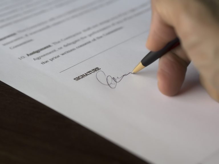 Gros plan sur la main d'un client signant sereinement un contrat commercial sur un bureau.