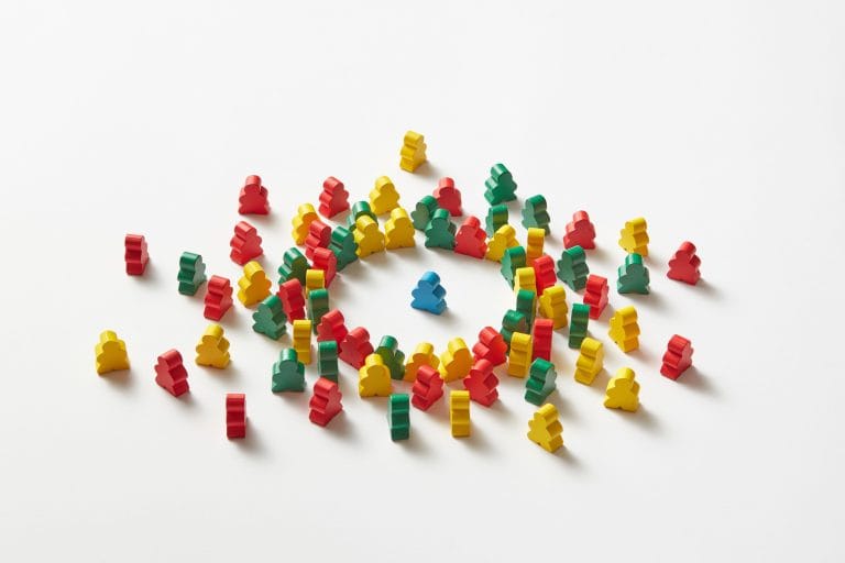 Photographie de figurines en bois colorées et désordonnées en cercle autour d'un unique personnage bleu central, symbolisant l'attraction et l'effet aimant d'un produit d'appel stratégique sur des prospects.