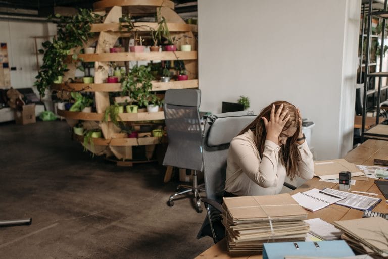 Dirigeante de PME débordée, seule à son bureau jonché de papiers et dossiers, illustrant le syndrome du dirigeant indispensable.